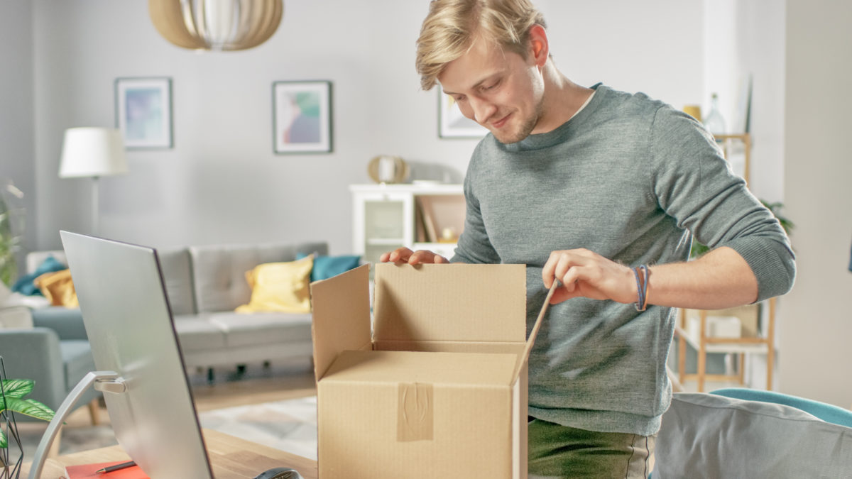 Blond haired White man opening a box with materials for a virtual reunion avtivity.